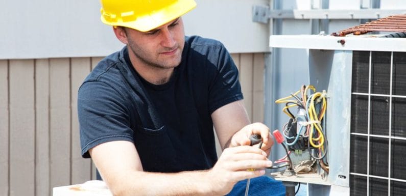 An HVAC Technician in a hardhat works on an air conditioning unit.