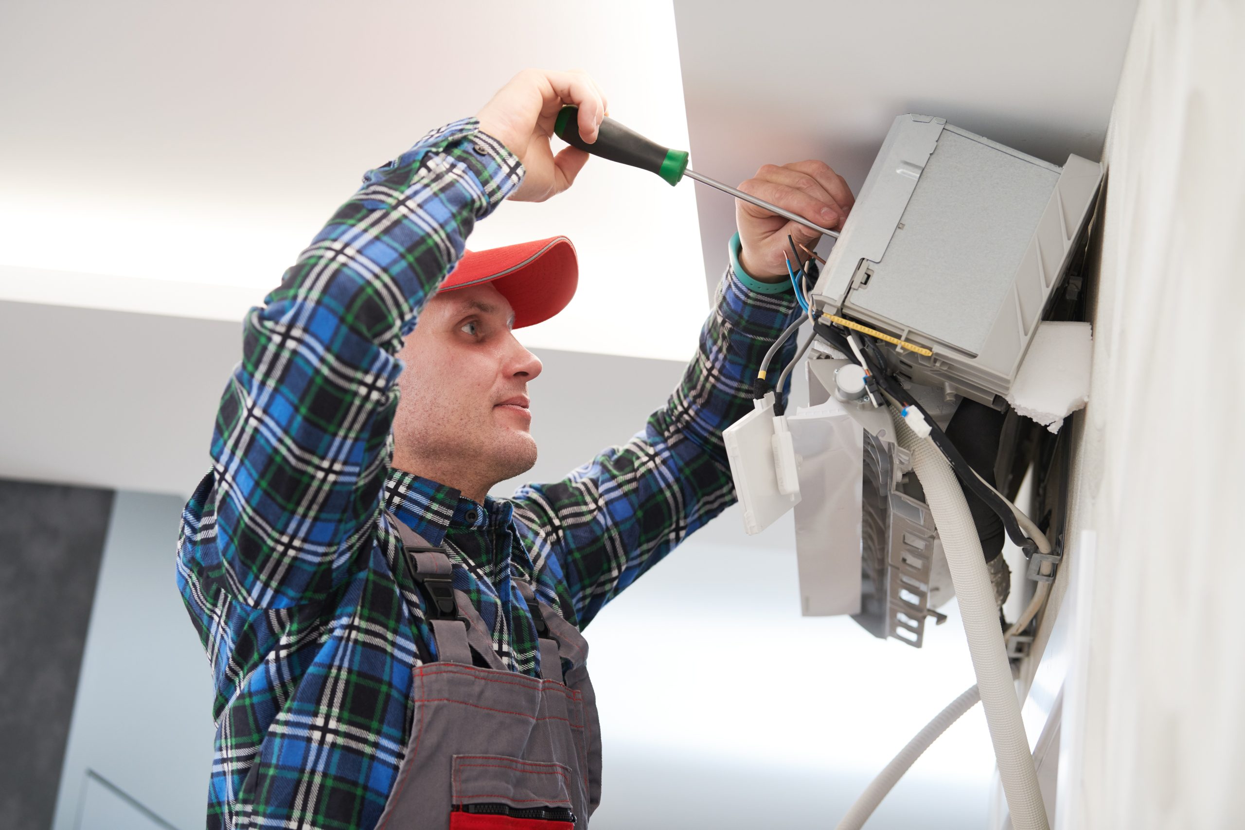 Man working on a air conditioning unit with a screw driver. 